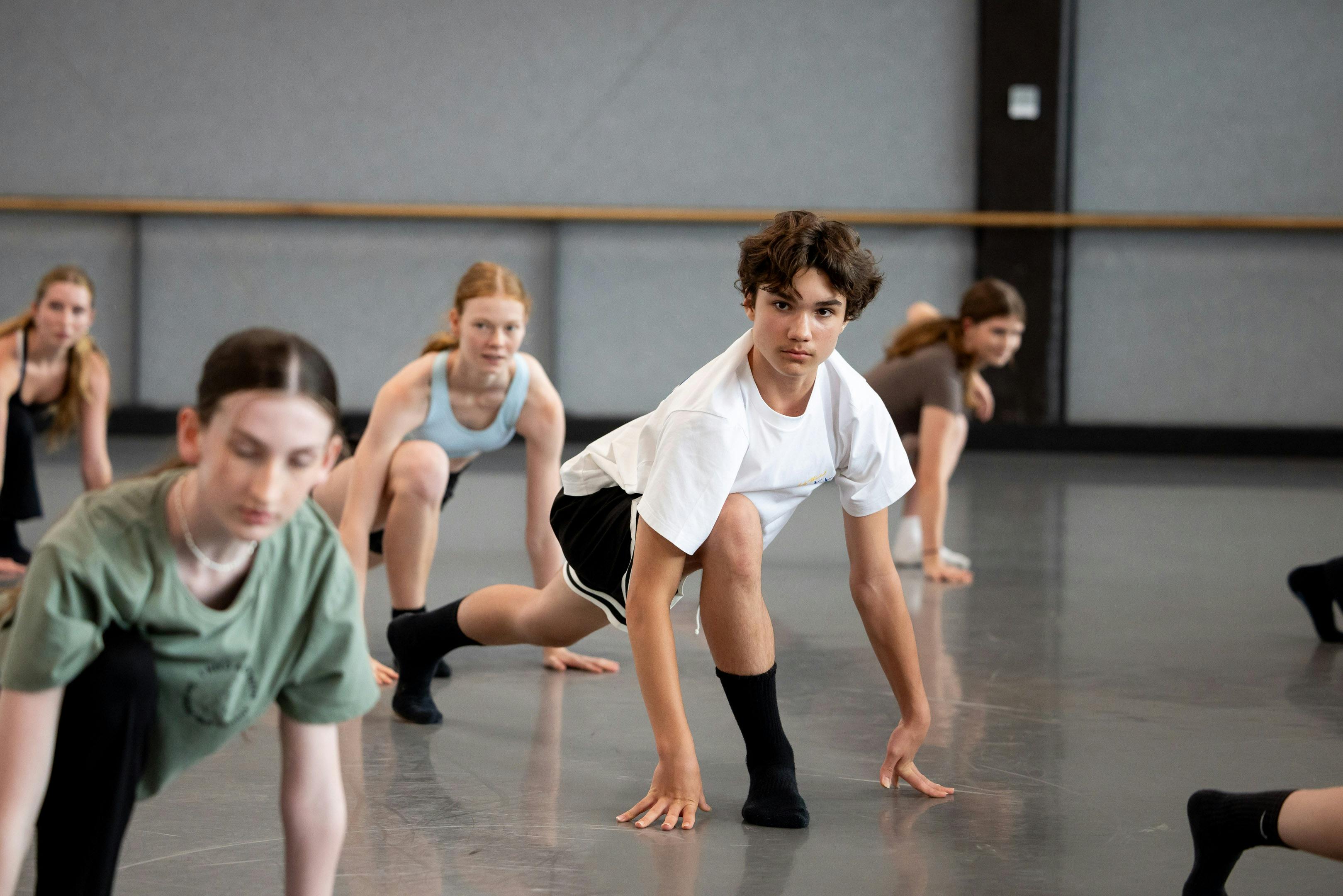 Young male (aged ~ 16-18) is dancing in a crouched position. There are other dancers around him.