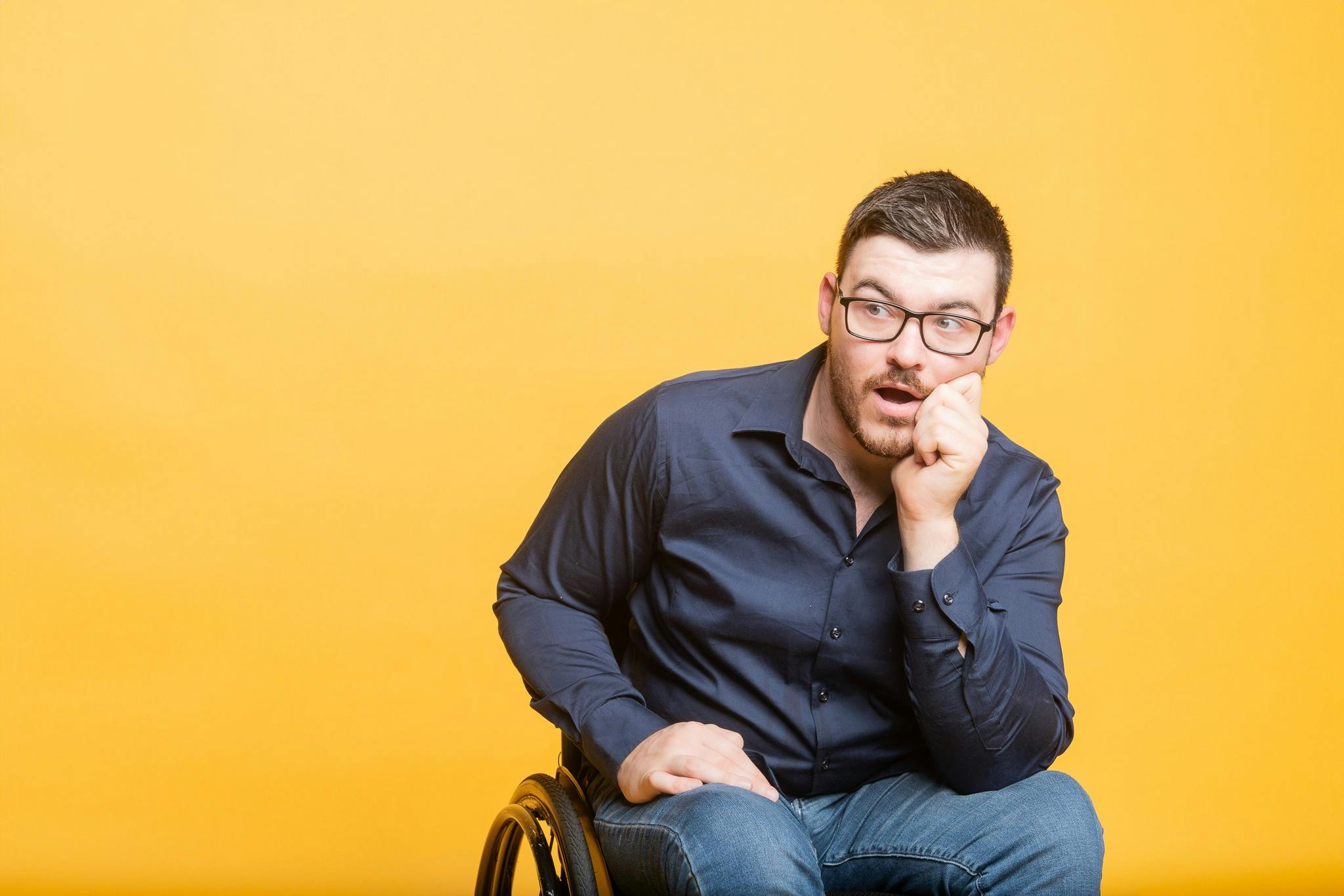 Comedian Oliver has short, dark hair is wearing glasses and is sitting in a manual wheelchair.
