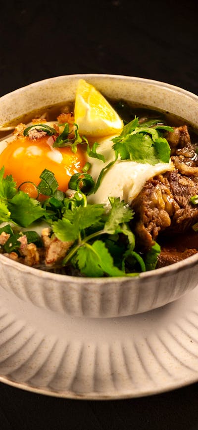 Beef Rawon soup served with egg, fresh herbs and a lemon wedge
