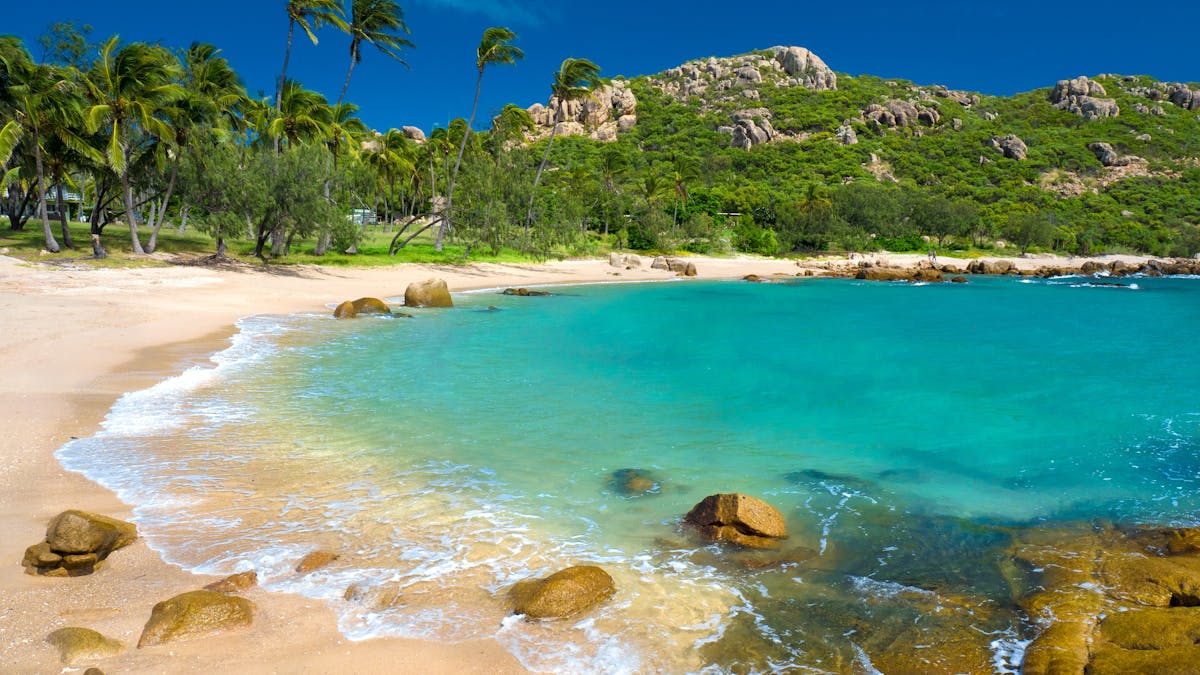 Sandy beach, blue water, palm trees and granite headlands Sandy beach, blue water, palm trees and granite headlands