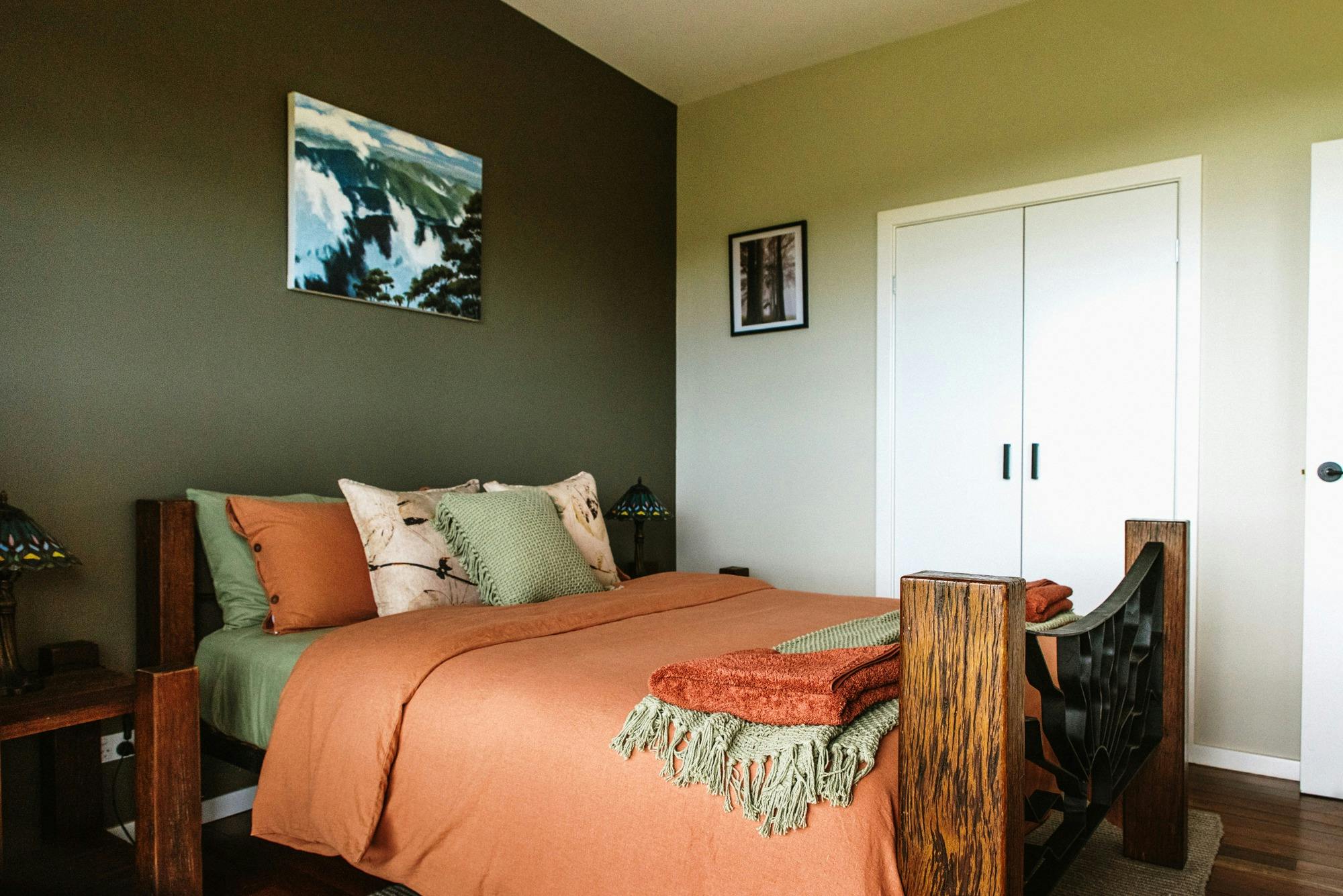Photo of bed n bedroom with rusty orange linen and sage and green pillows and green walls