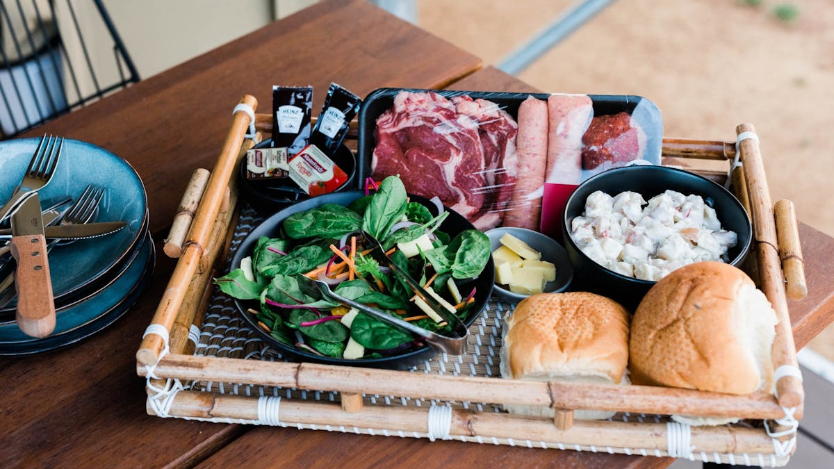 Bamboo tray with meats, salad and bread rolls on outdoor table
