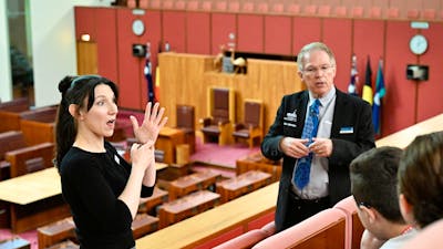 Parliament House tour guide explains the Senate chamber to visitors while an Auslan guide interprets