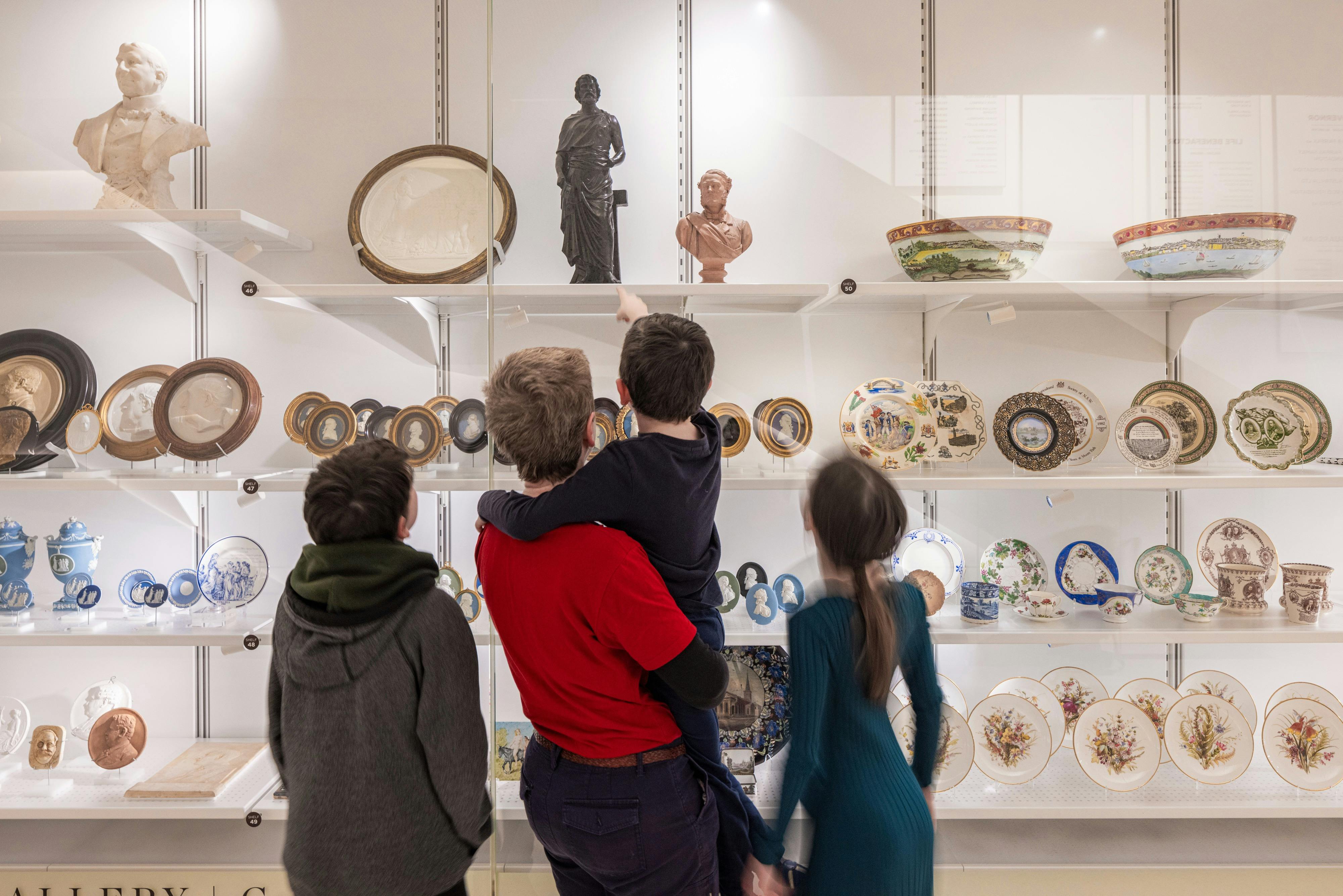 Ein Vater mit drei Kindern steht vor einer Vitrine voller kurioser Objekte