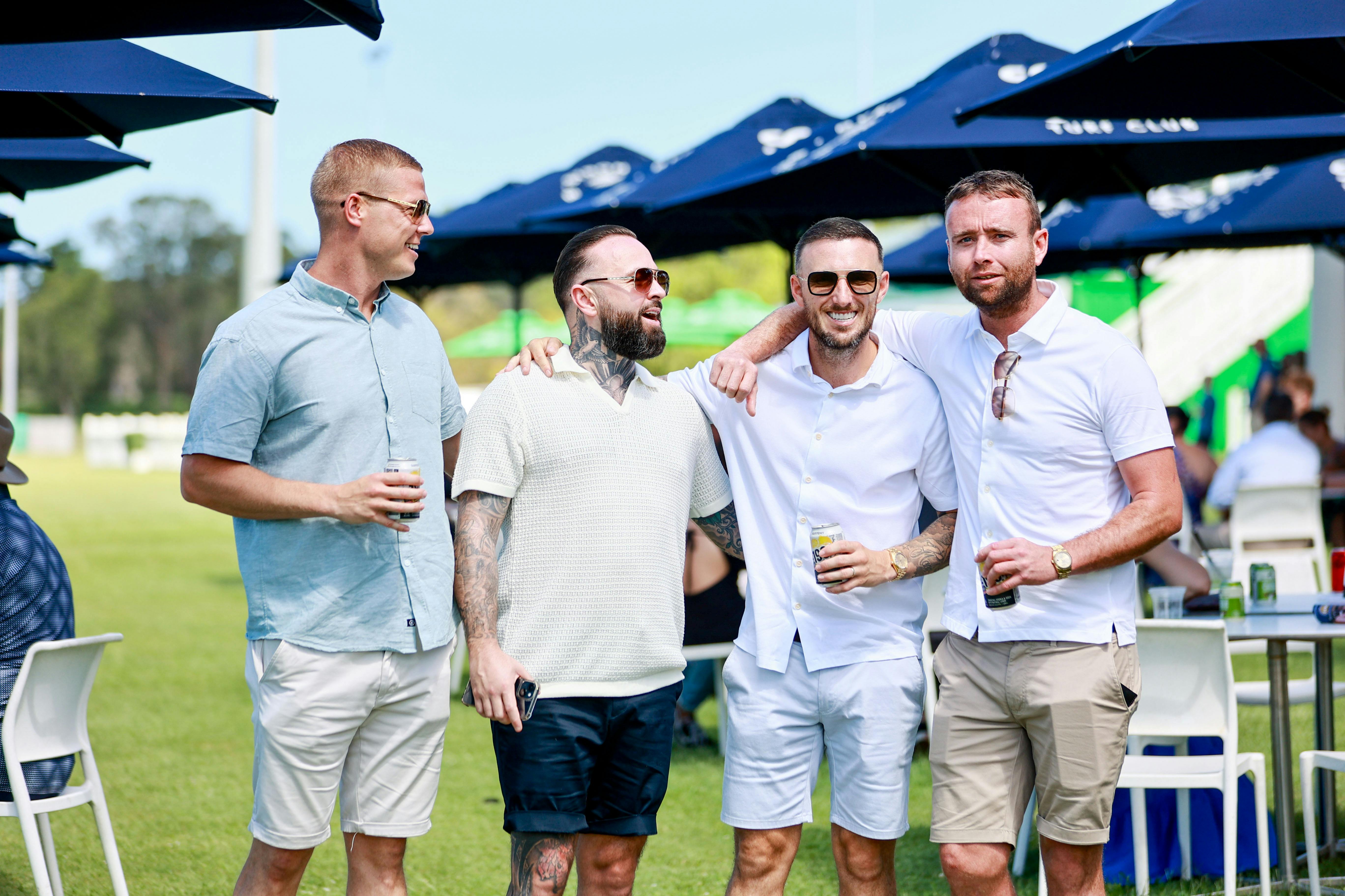 Group of four men on the front lawn under holding a beer and smiling at each other
