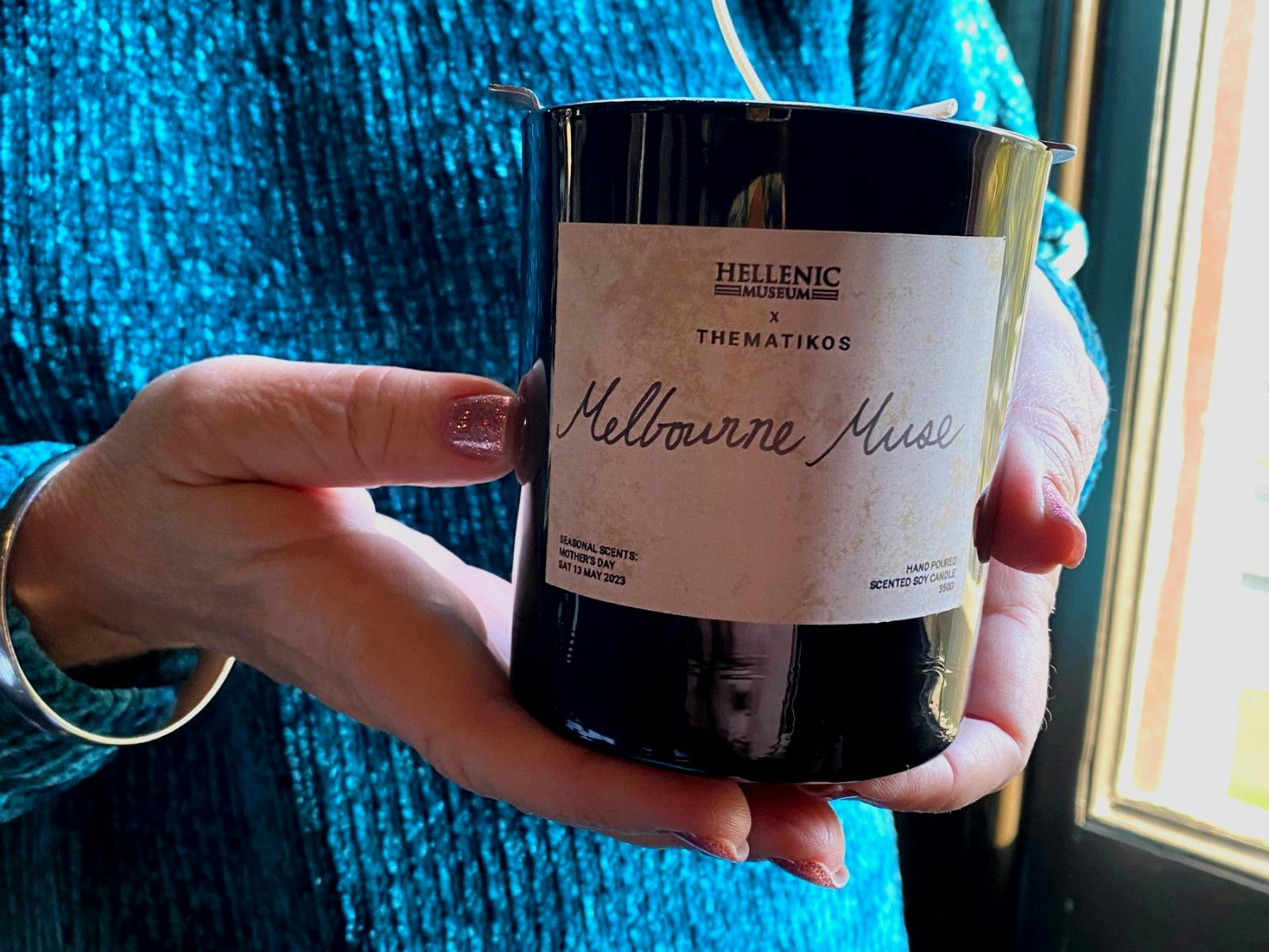 Cropped photo of a woman's hands holding a 'Melbourne Muse' candle with handwritten label