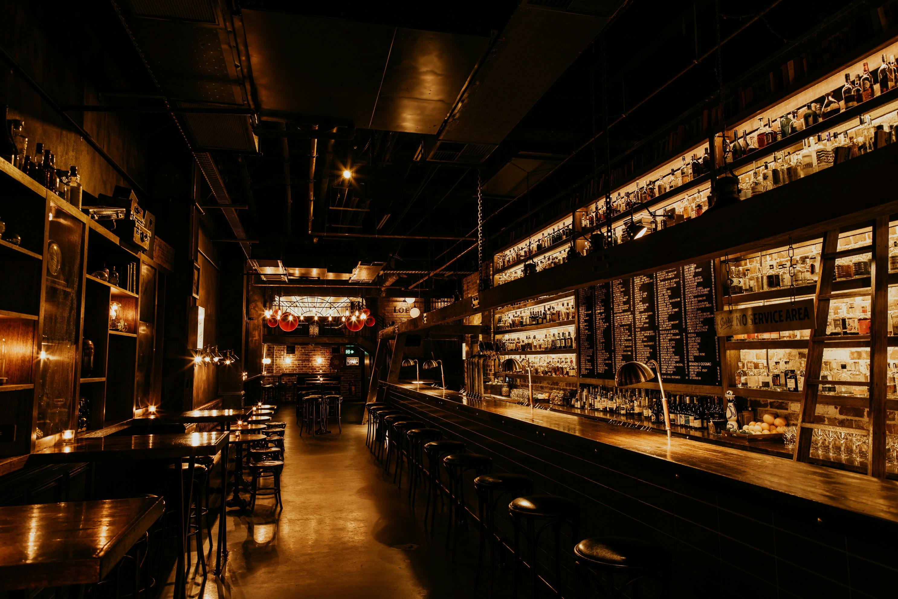 Low Lit bar with high shevles is pictured with spirits on the shelves