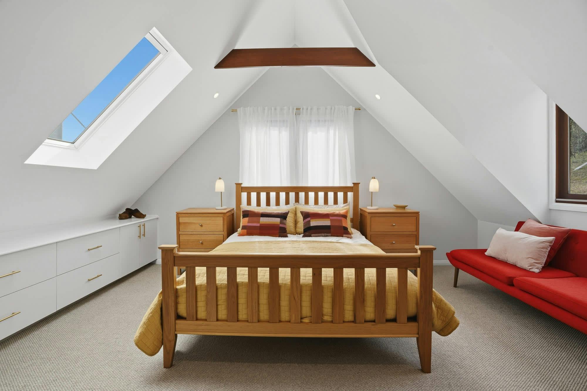 Queen bed with dark wooden furniture, angled ceilings and sunlights