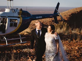 Couples in wedding attire standing next to parked helicopter on a hill