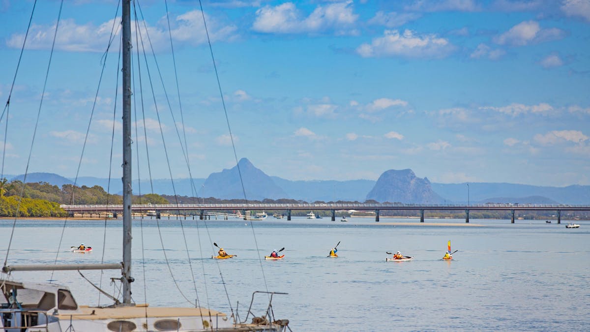 Five kayaks in the shallow waters heading away from Bribie Island bridge