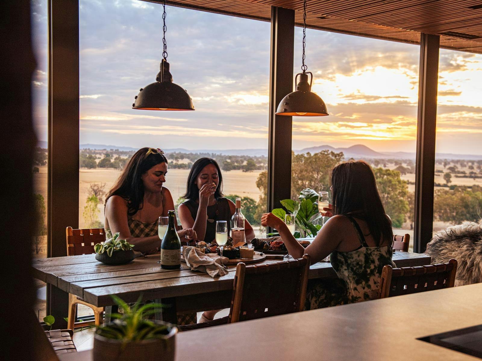 Ladies sitting at a rustic table with views across valley at sunset