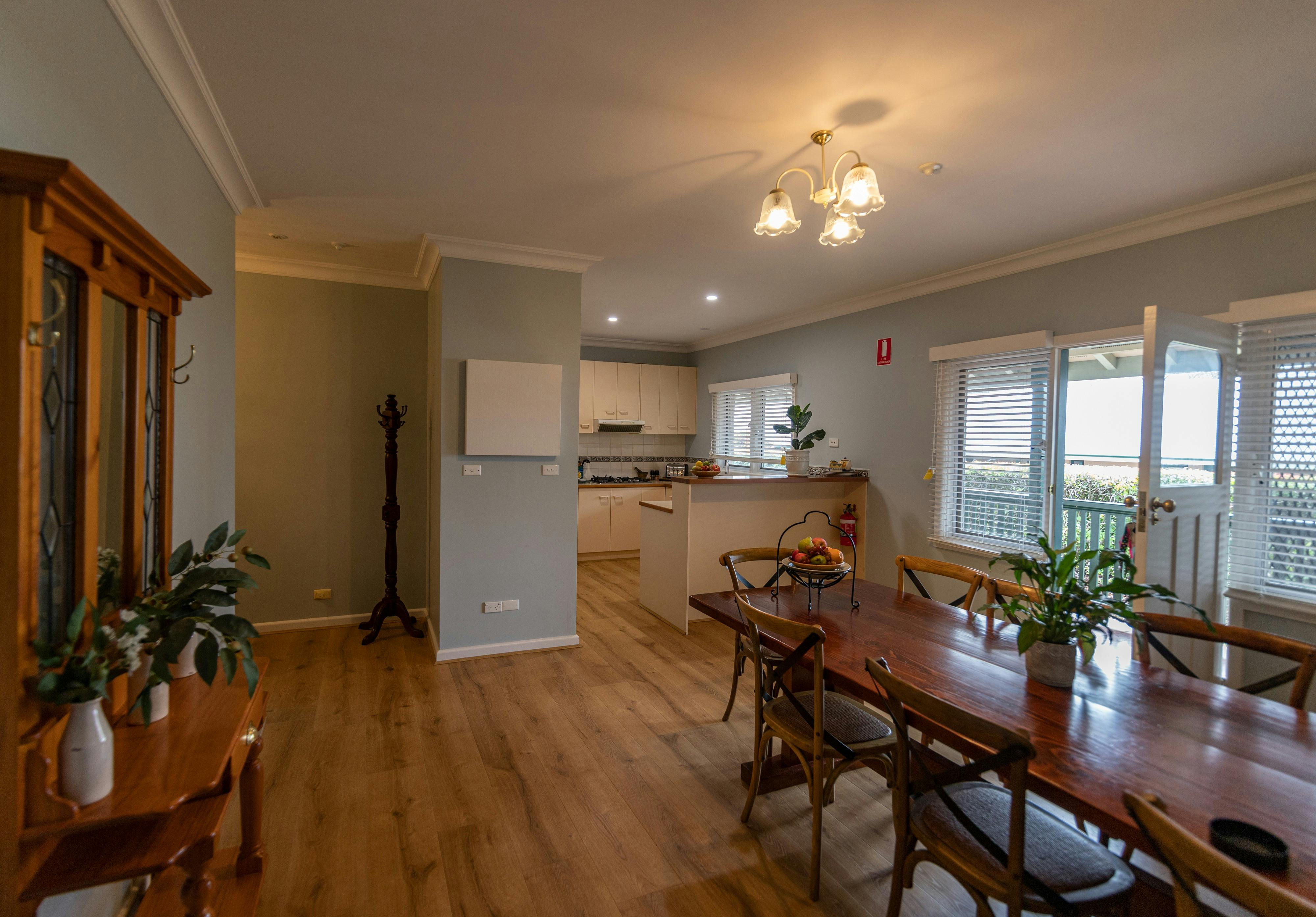 A cozy dining space with a wooden table, open kitchen, and warm lighting, leading to a veranda