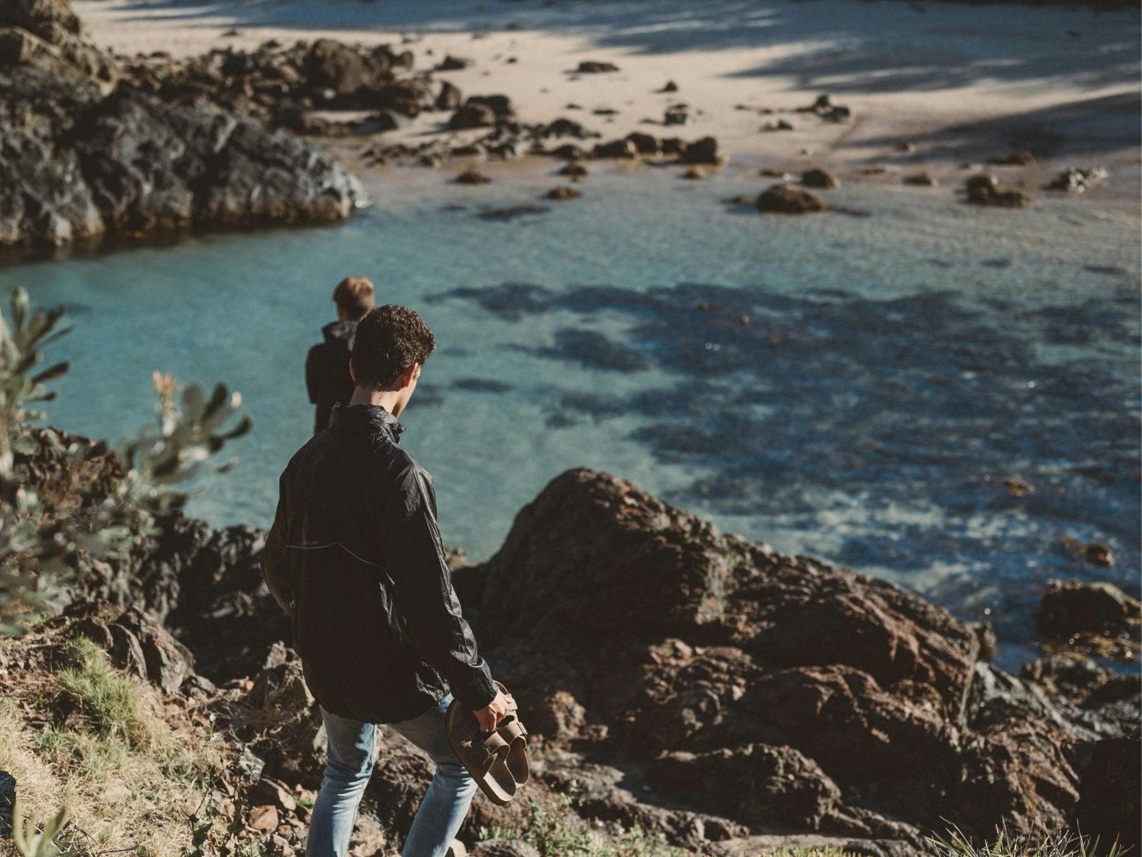 Two men, walking down rocks to a beach