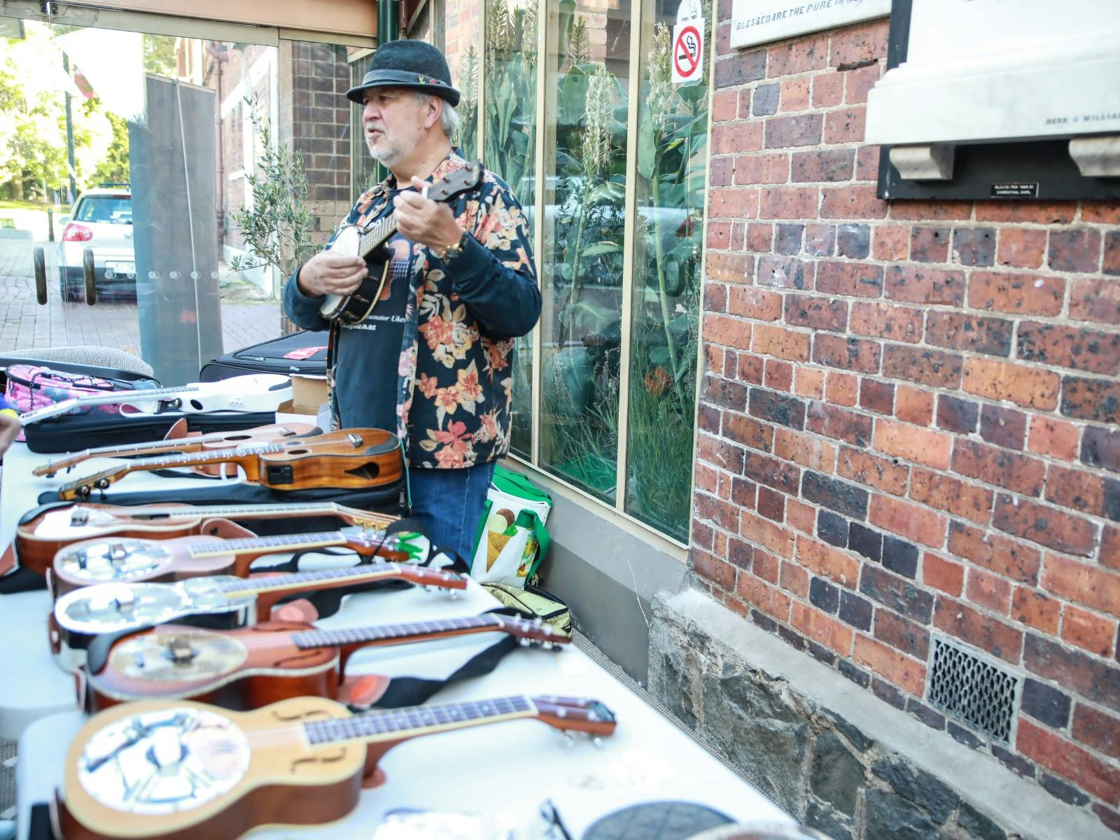 Table displaying a range of ukuleles including resonator style. Luthier standing behind stall.