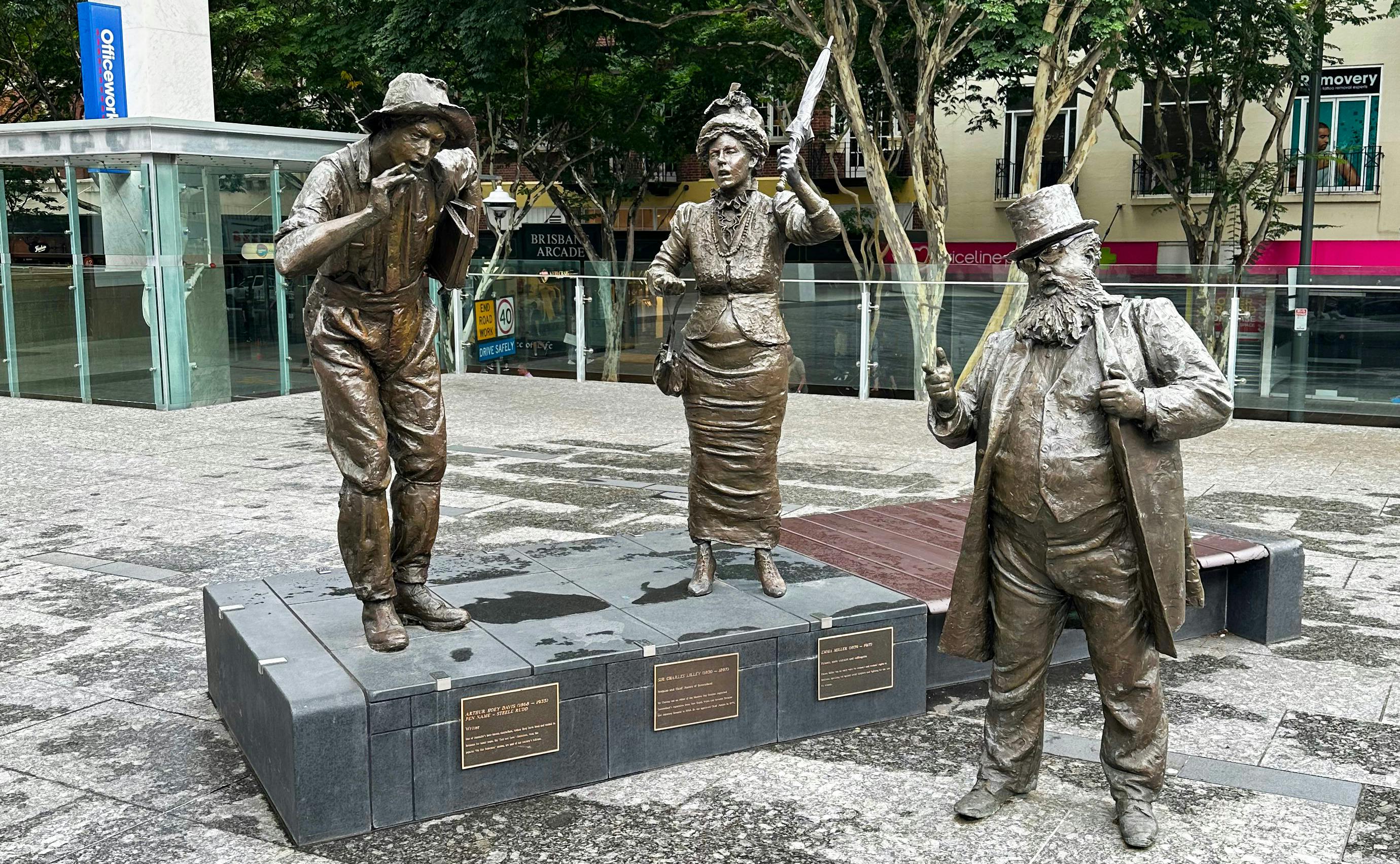 Statue of 3 people. Two men in hats and a lady holding an umbrella