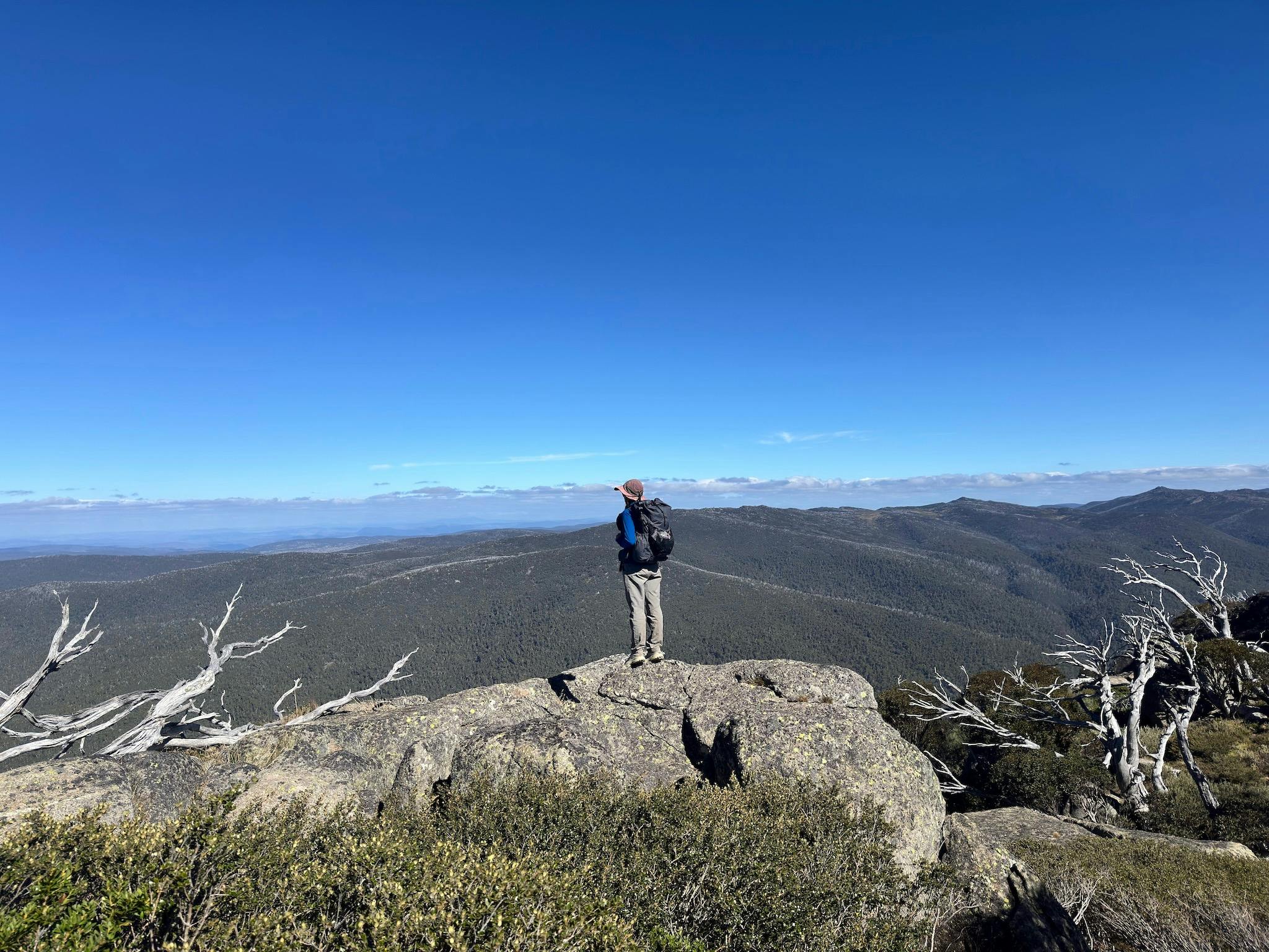 A hiker standing on a rock and looking out at the mountain view.