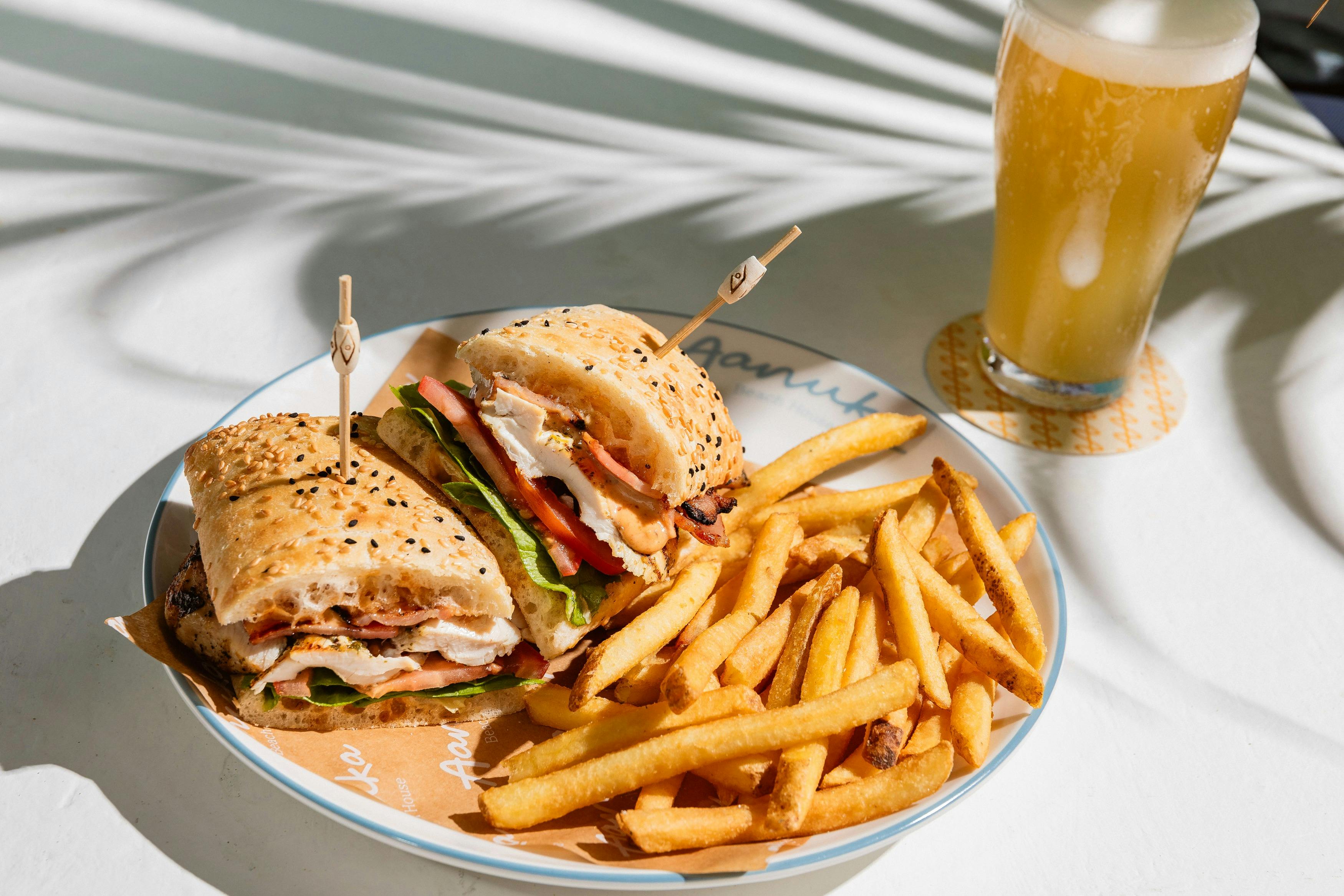 A chicken club sandwich paired with a schooner of beer.