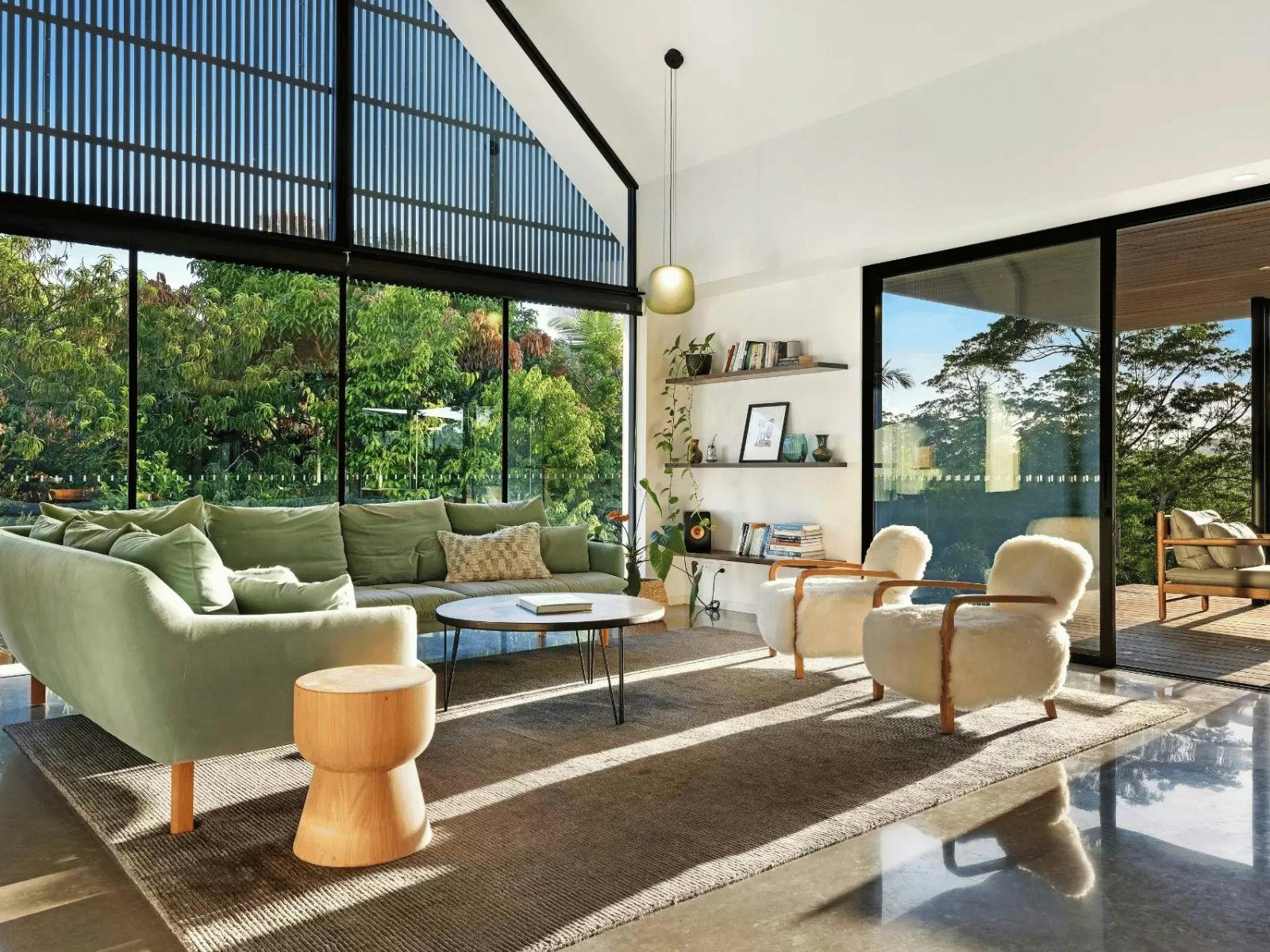 Modern living room with floor to ceiling glazing opening onto a timber deck and gardens.
