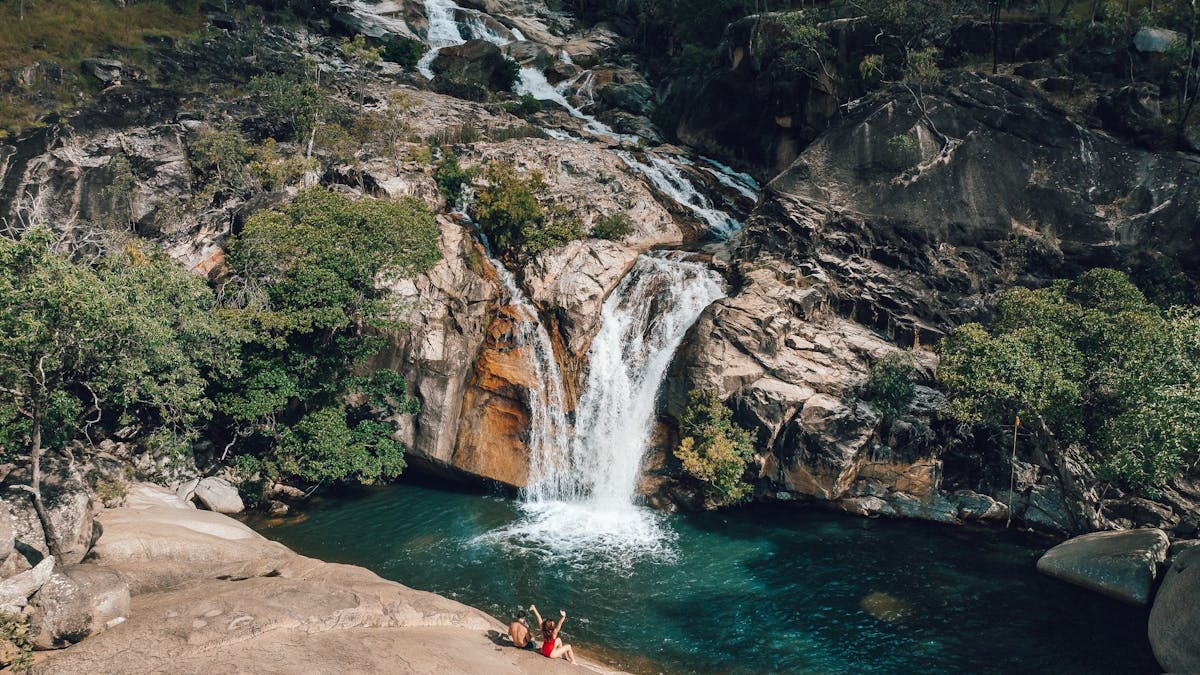 A couple sit on a granite boulder overlooking the waterfalls at Emerald Creek Falls in Mareeba TNQ.