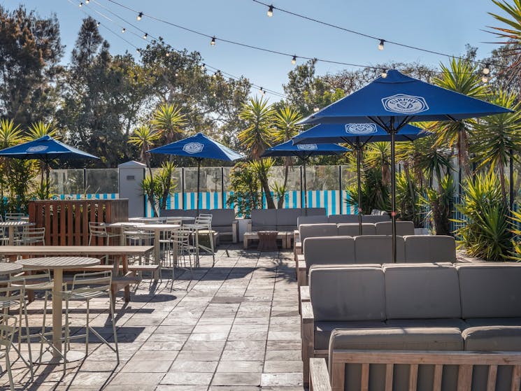 Paved outdoor courtyard with outdoor tables and chairs and large  blue umbrellas