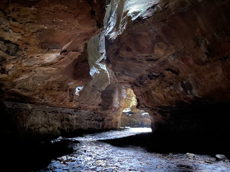 A dark sandstone walled slot canyon with dappled sunlight streaming down from above.