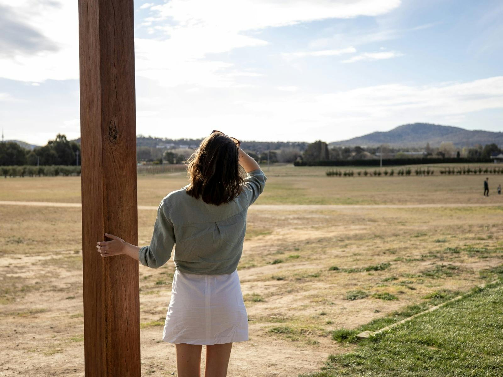 A tourist stands at a lookout, viewing vast open bush-covered fields stretching into the distance.