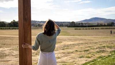 A tourist stands at a lookout, viewing vast open bush-covered fields stretching into the distance.