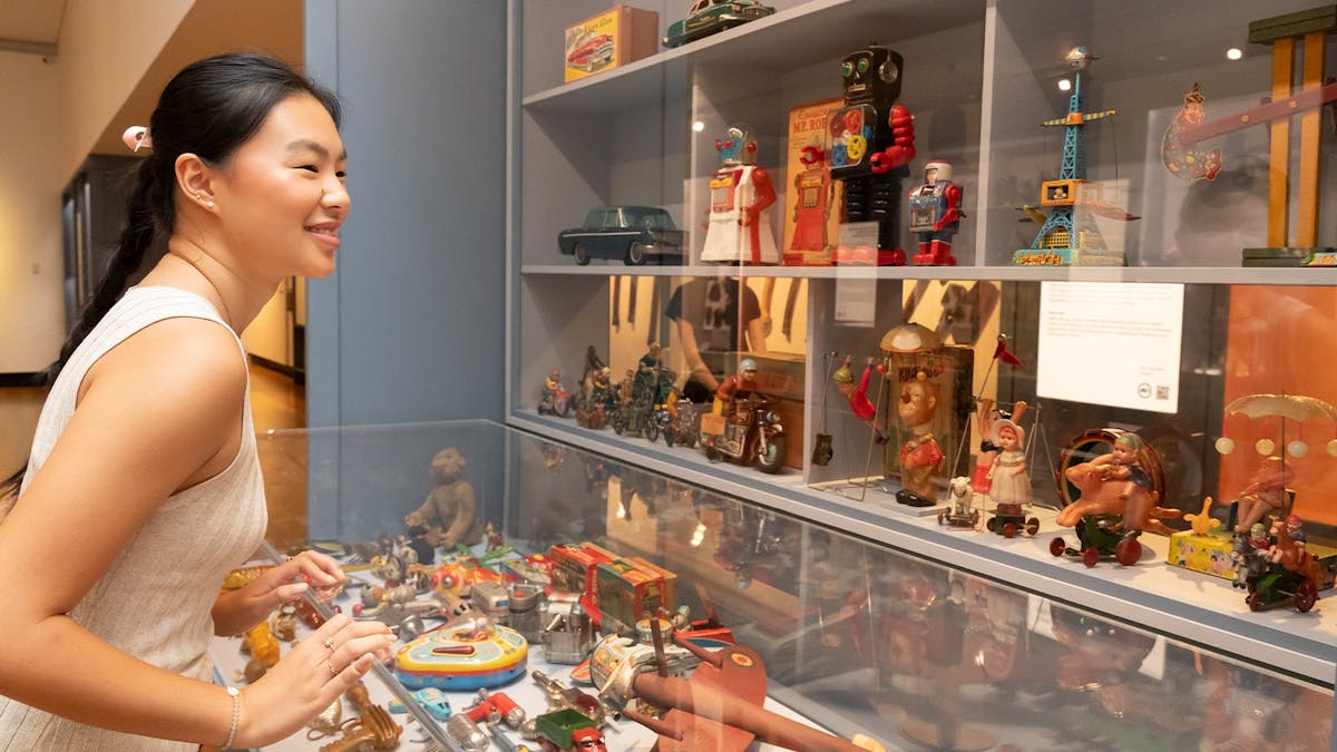 Woman looking at a cabinet of vintage toys, smiling.