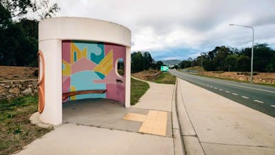 A picture of A Canberra Bus Stop with A painted internal artwork with blue yellow and pink