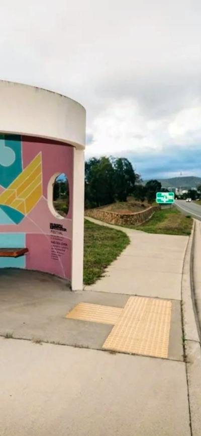 A picture of A Canberra Bus Stop with A painted internal artwork with blue yellow and pink