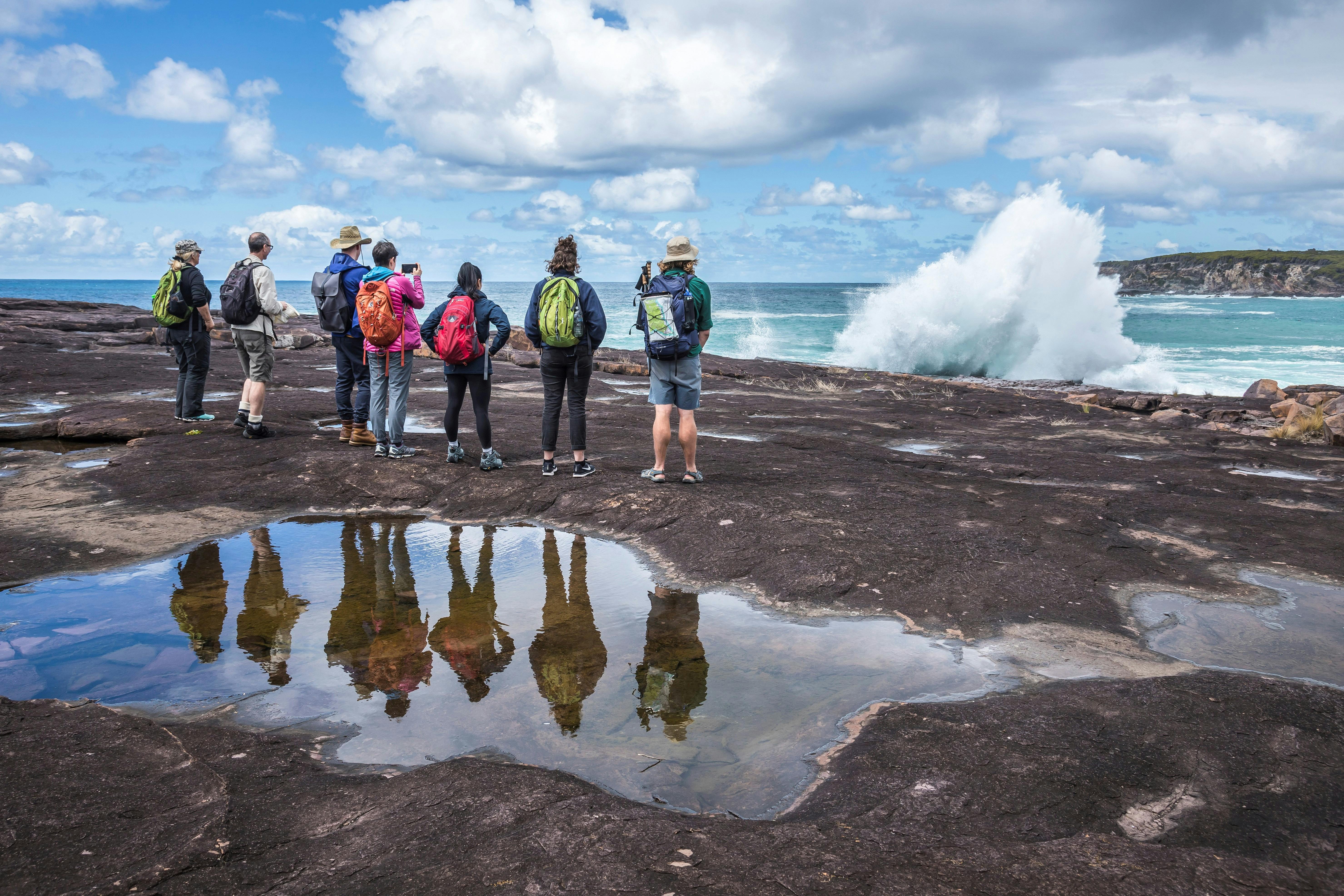 Walkers watch a wave crash on cliffs on the Light to Light walk