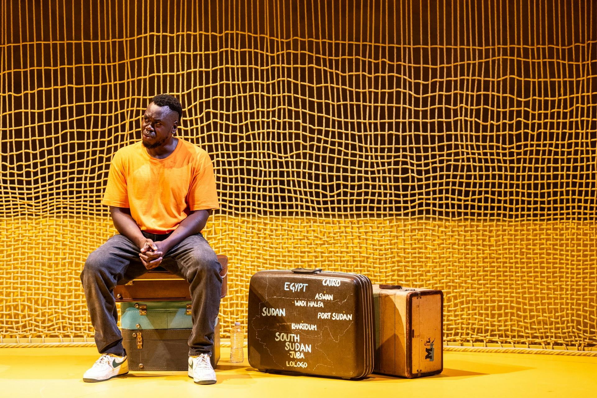Man sitting on old luggage cases, one with a painted map of Africa including South Sudan map