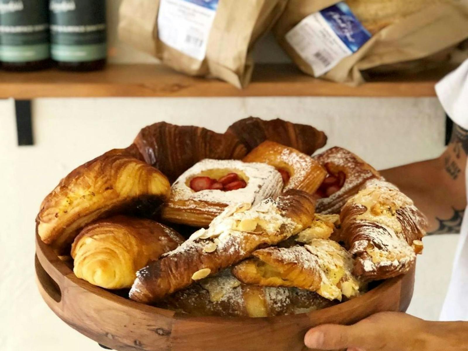 Image of various pastries dusted with icing sugar and displayed on a round timber board