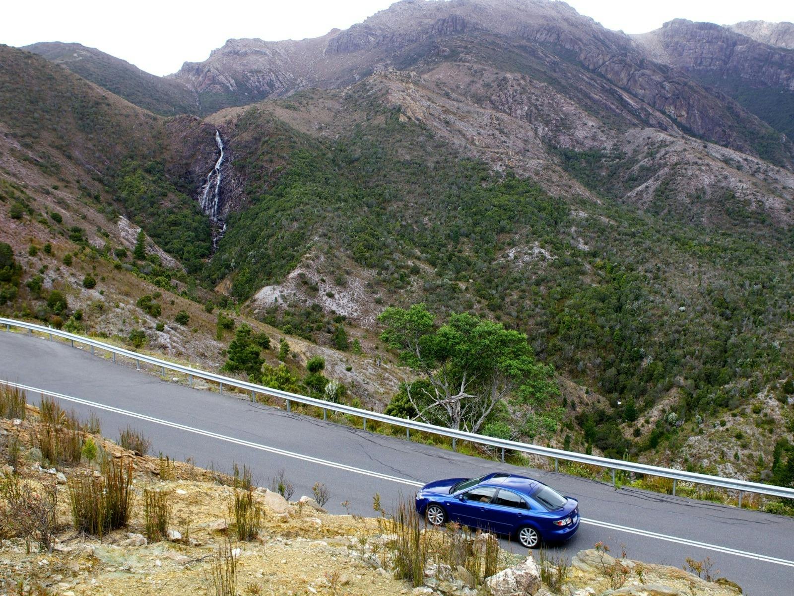 A car drives uphill with a clear waterfall visible ahead