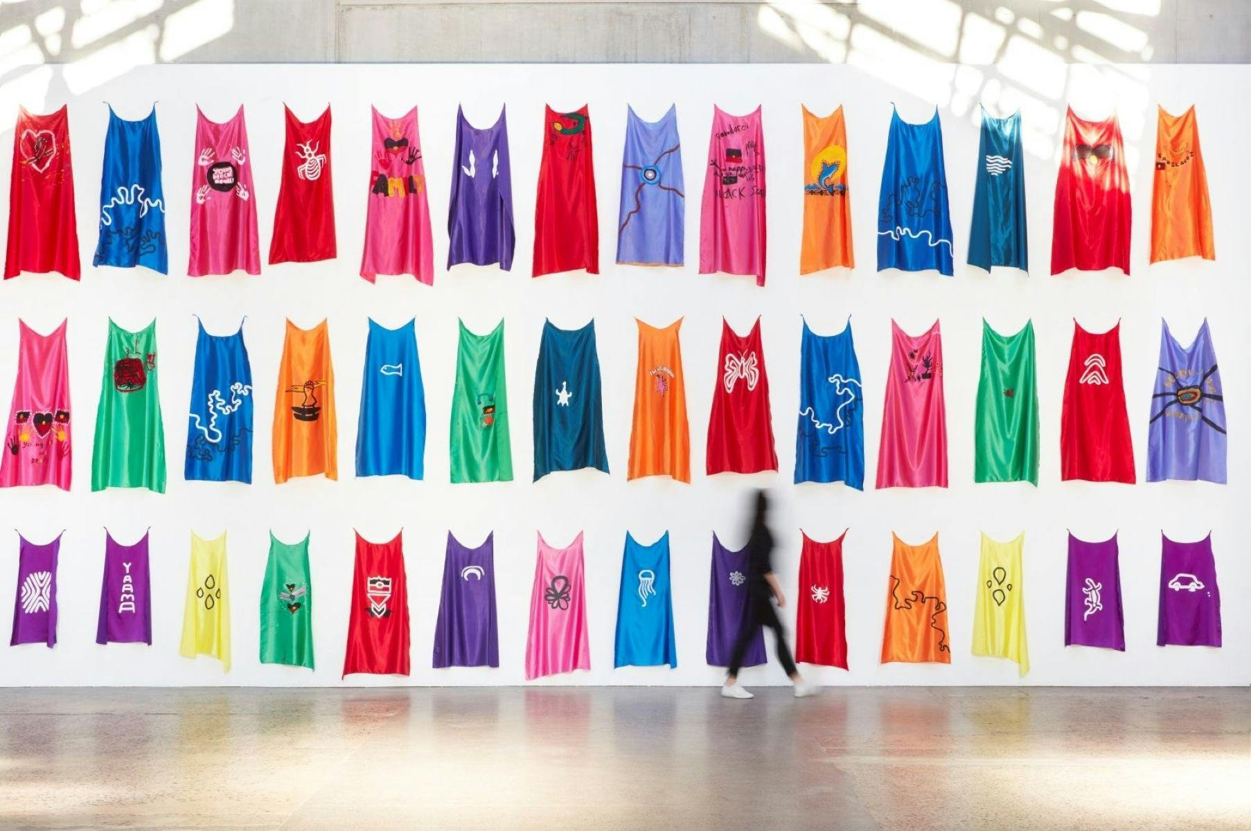 Colourful installation of capes showing various playful symbols and emblems.
