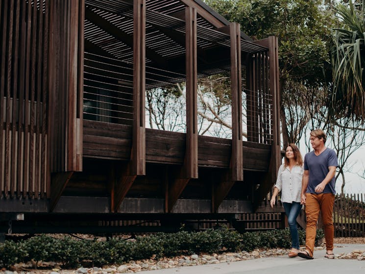 Two people holding hands walking past a modern, wooden cabin