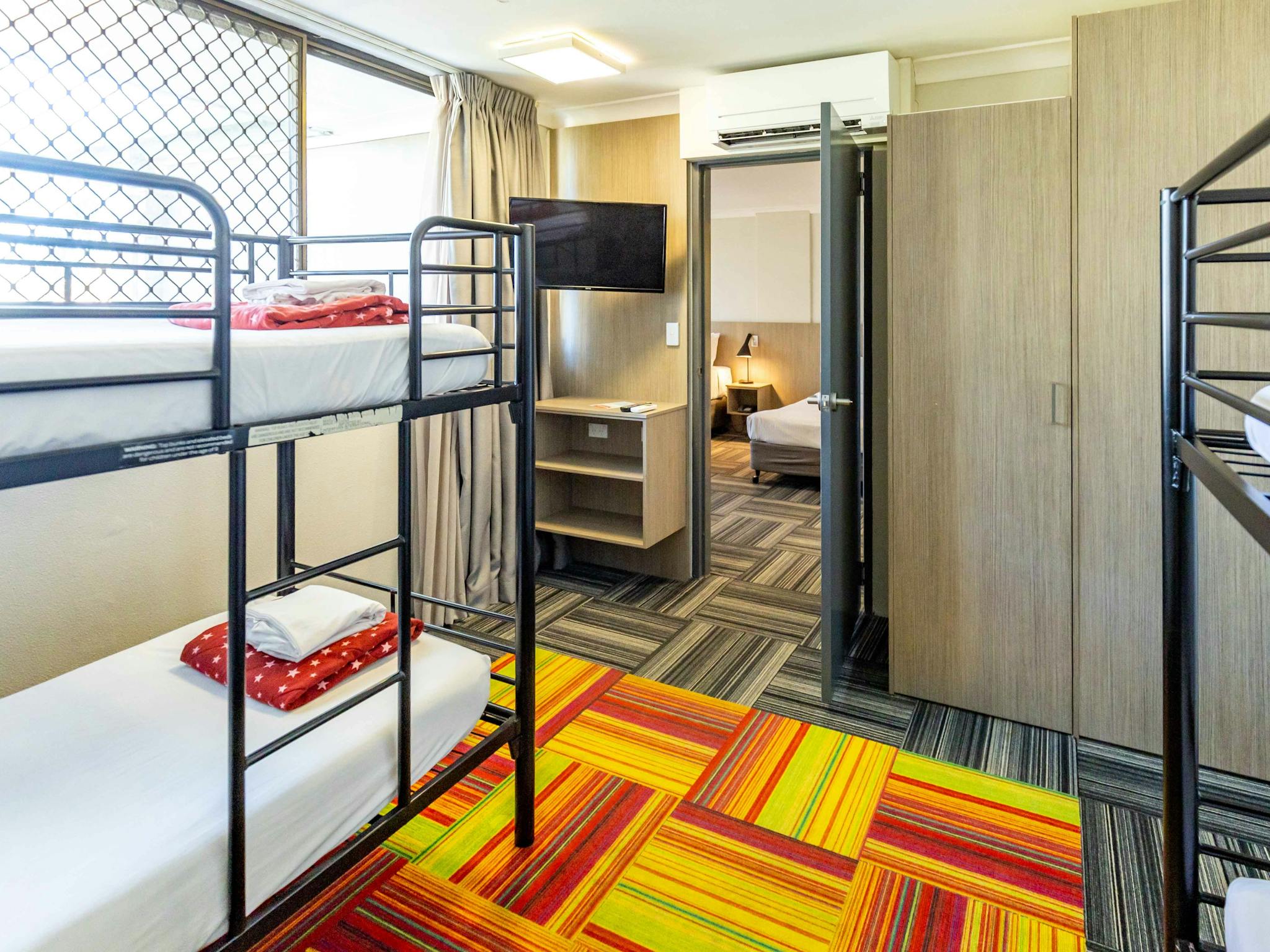 Two sets of bunks with a TV and set of shelves with a door open to another room and part of a bed Two sets of bunks with a TV and set of shelves with a door open to another room and part of a bed