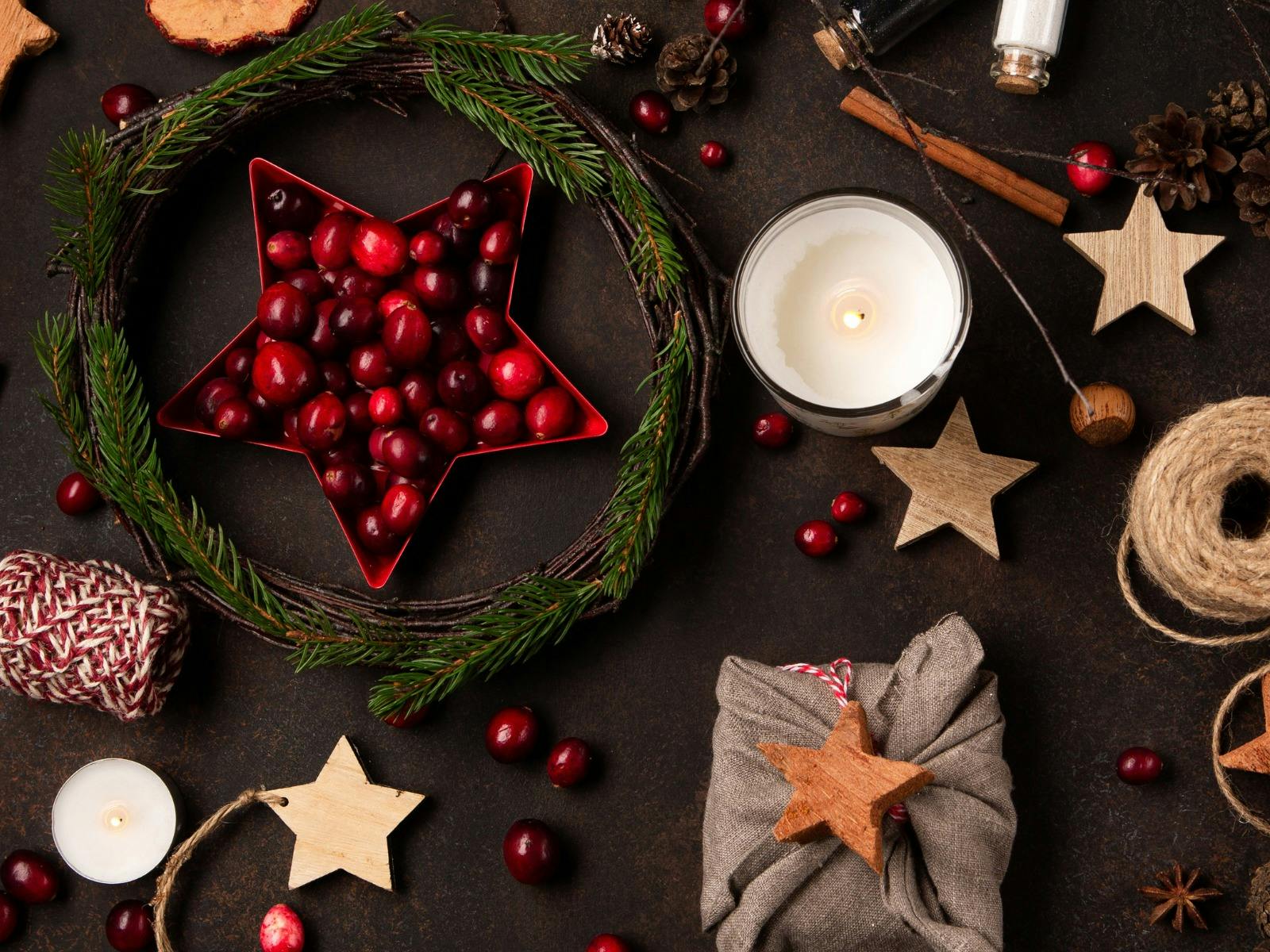 A flat lay image of Christmas related aromatics, candles and gift wrapping sitting on a dark surface