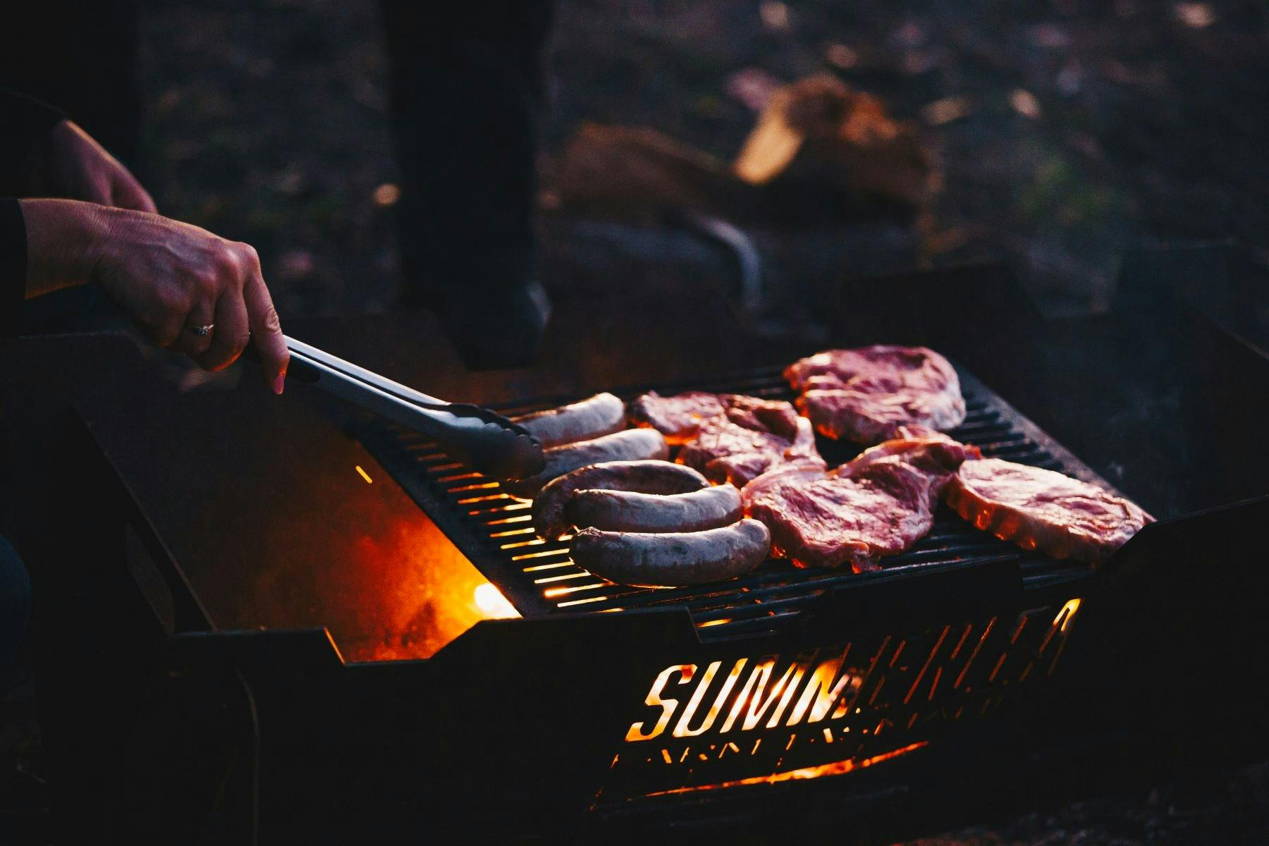 steaks and sausages cooking over open fire