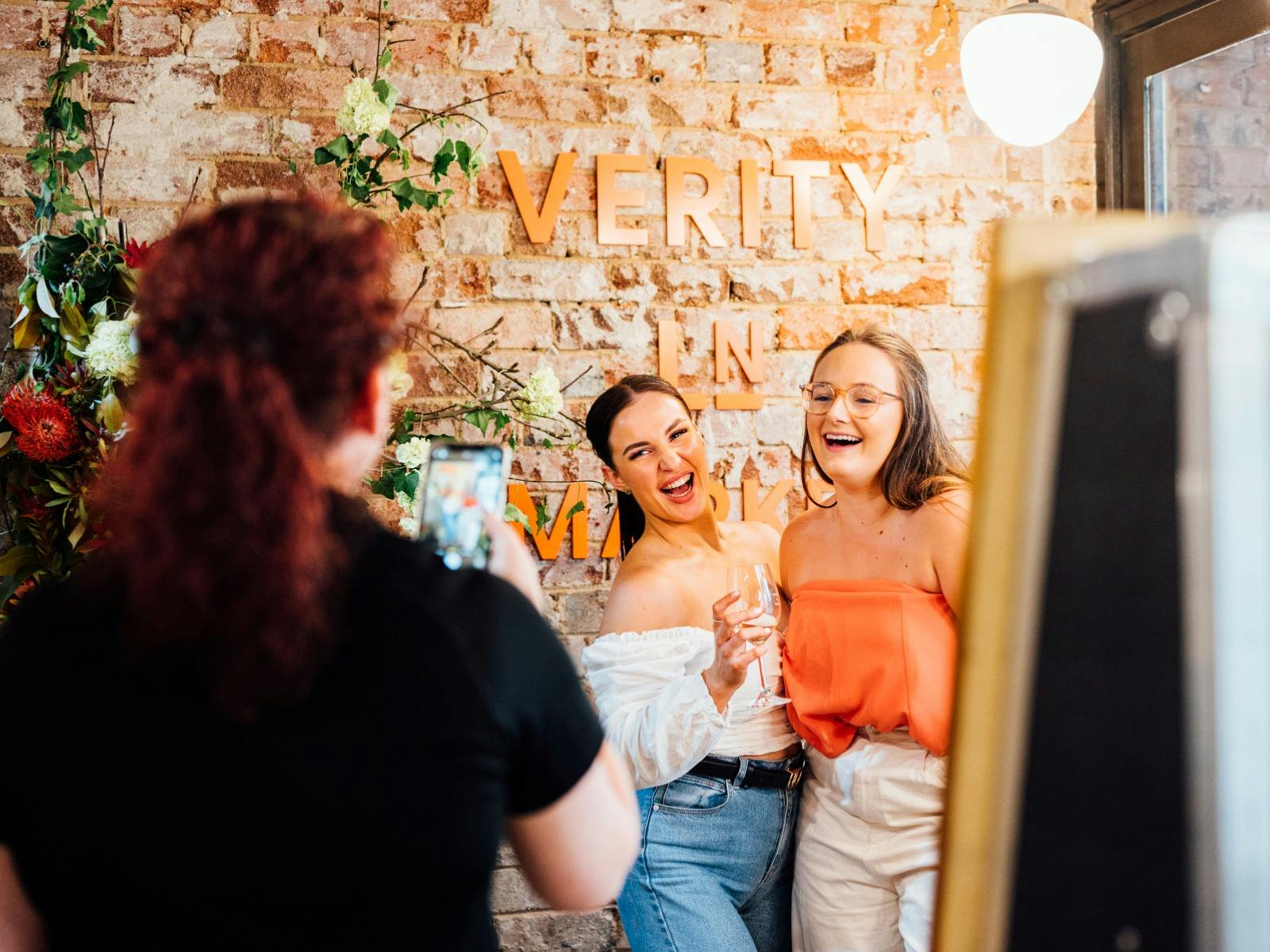 People taking photo in front of Verity Lane Market logo next to flowers