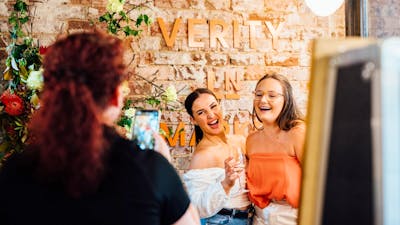 People taking photo in front of Verity Lane Market logo next to flowers