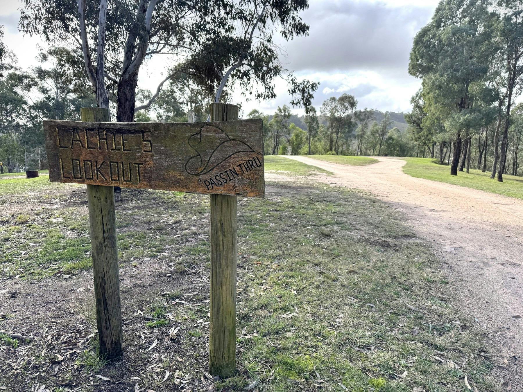 Á timber sign with yellow writing says Lachies Lookout stands in front of a grassed area and road
