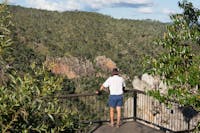 Person stands at lookout with views over forested slope and waterfall.