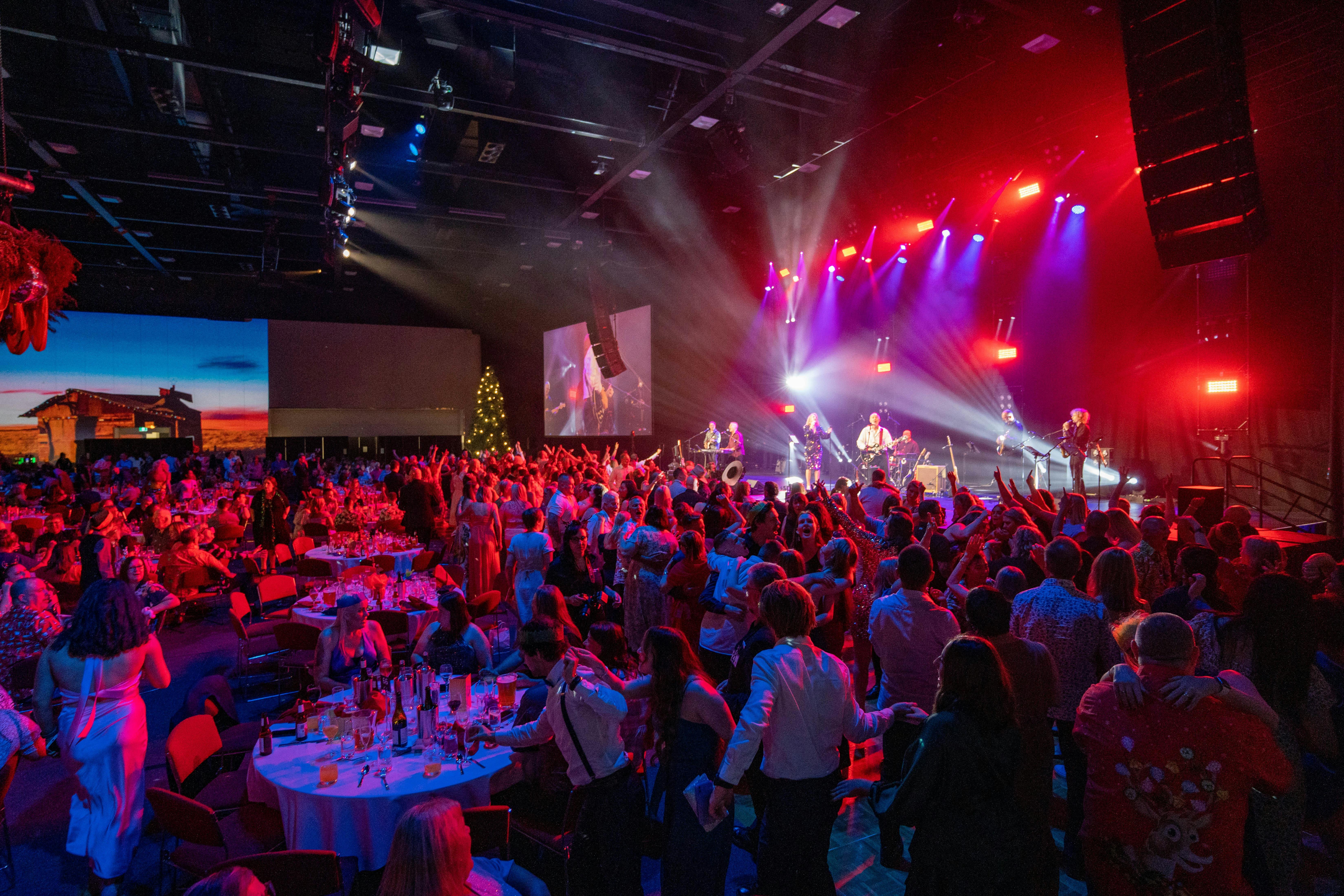 Image of an event hall with banquet tables and people sitting, with an event stage in the background