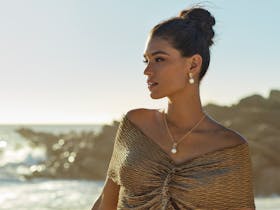 Our muse looks out at the horizon whilst wearing our pearl Bloom collection. It is sunset.