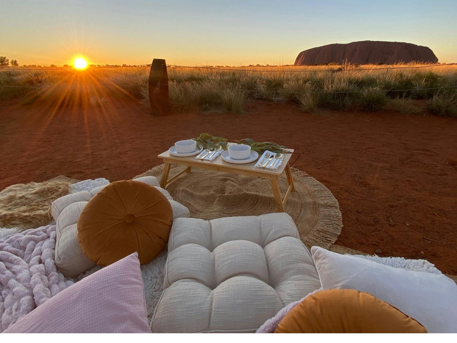 Picnic with cushions and rugs with Uluru in Background