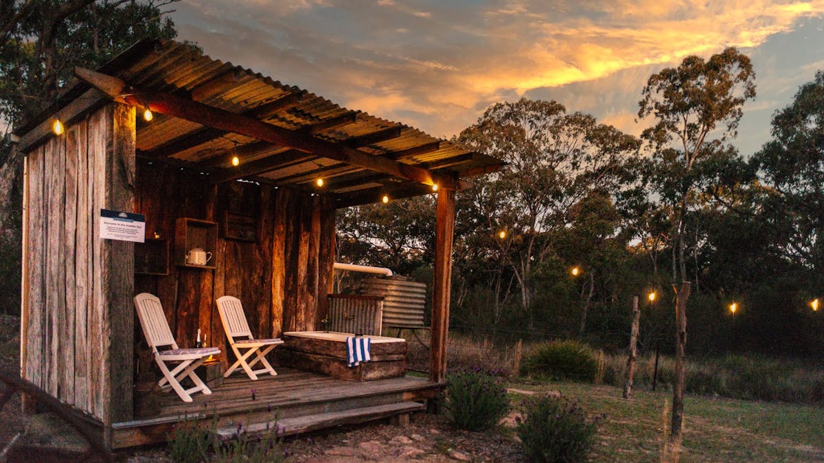 outdoor bath tub situated on timber structure, festoon lighting above and firepit