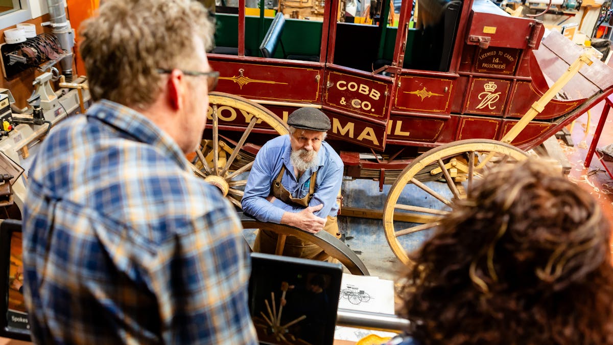 Factory worker talking to visitors with Cobb & Co coach in the background