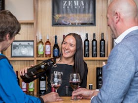 Young lady gives man and woman wine tasting in cellar door