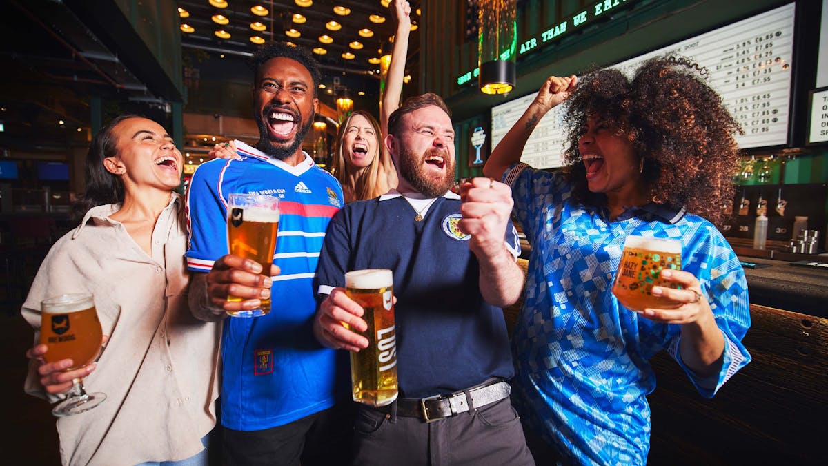 Friends in football jerseys cheering with beers in hand Friends in football jerseys cheering with beers in hand